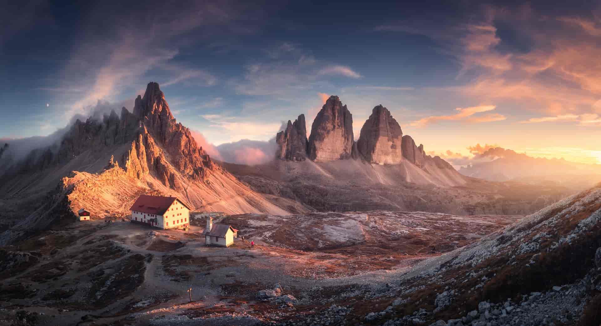 Mountains in Tre Cime park in Dolomites at sunrise with mountain huts below.
