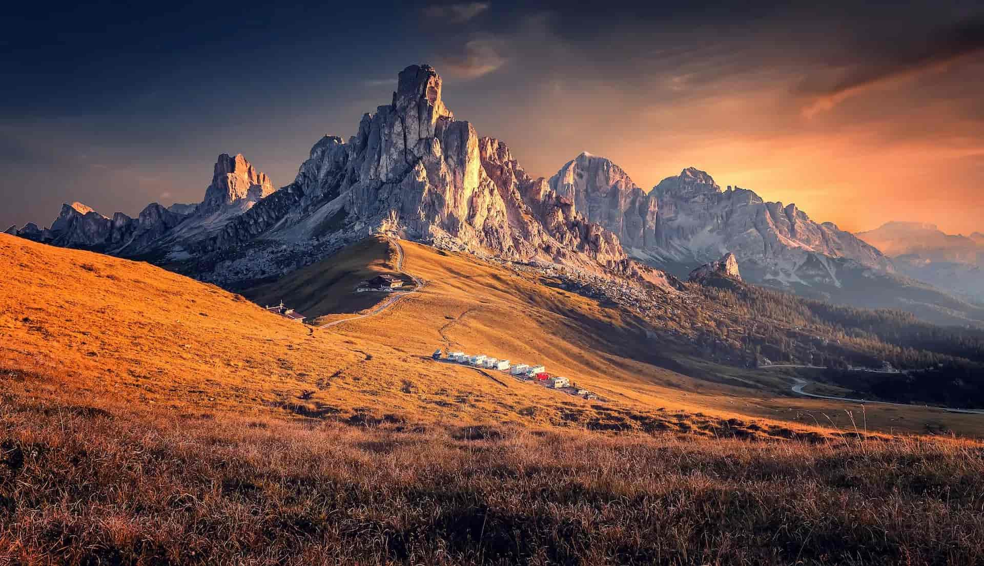 Rocky mountain peaks illuminated by sunset over golden grassy slopes at Passo Giau.