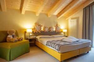 Cozy hotel bedroom with yellow bed frame, green sofa, and teddy bear under a wooden sloped ceiling.