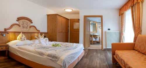 Hotel bedroom with wooden furniture, neatly made bed with towel swans, and orange sofa.