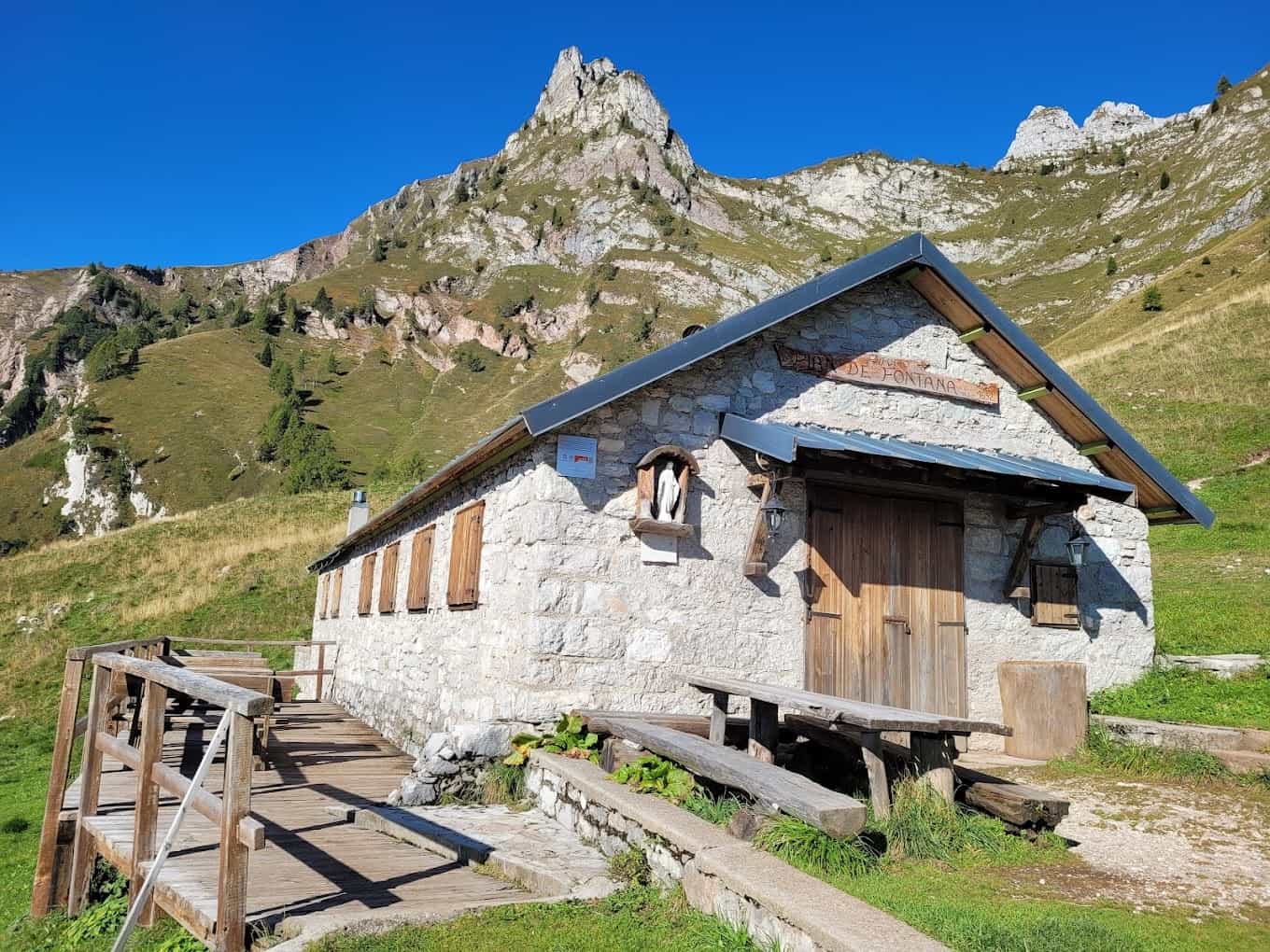 Rifugio Pian de Fontana stone mountain hut with wooden deck against grassy alpine slopes