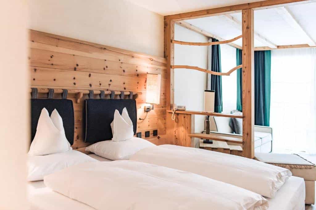 Hotel room with twin beds, white linens, and rustic wooden wall paneling and shelving.