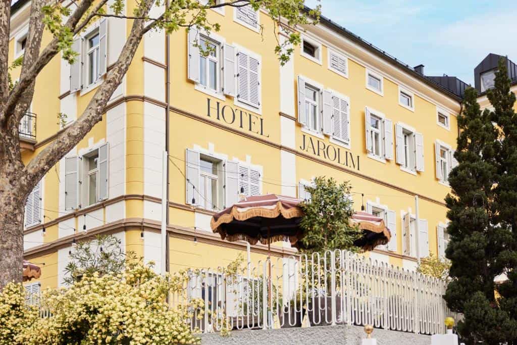 Yellow Hotel Jarolim building exterior with white shutters, outdoor seating, and spring foliage.