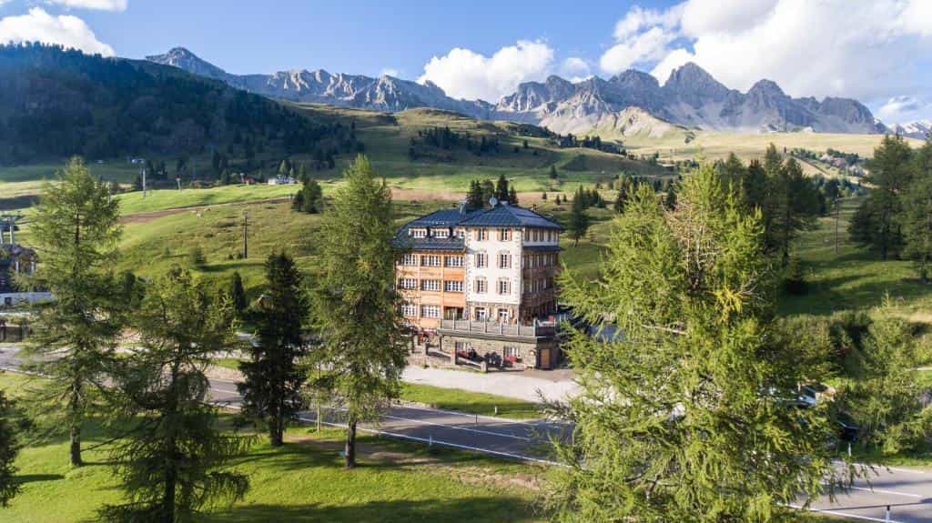 Hotel Costabella building nestled in green alpine foothills with rugged mountains in background