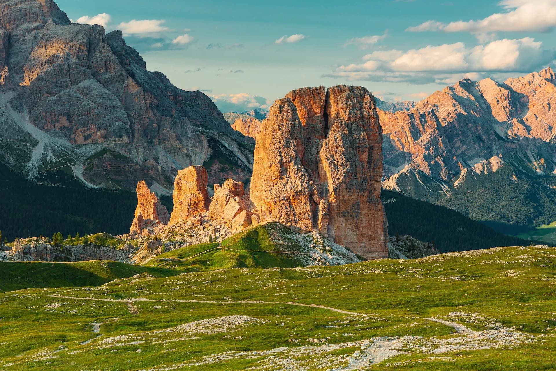 Cinque Torri rock formations illuminated by sun above green alpine meadow with hiking trails