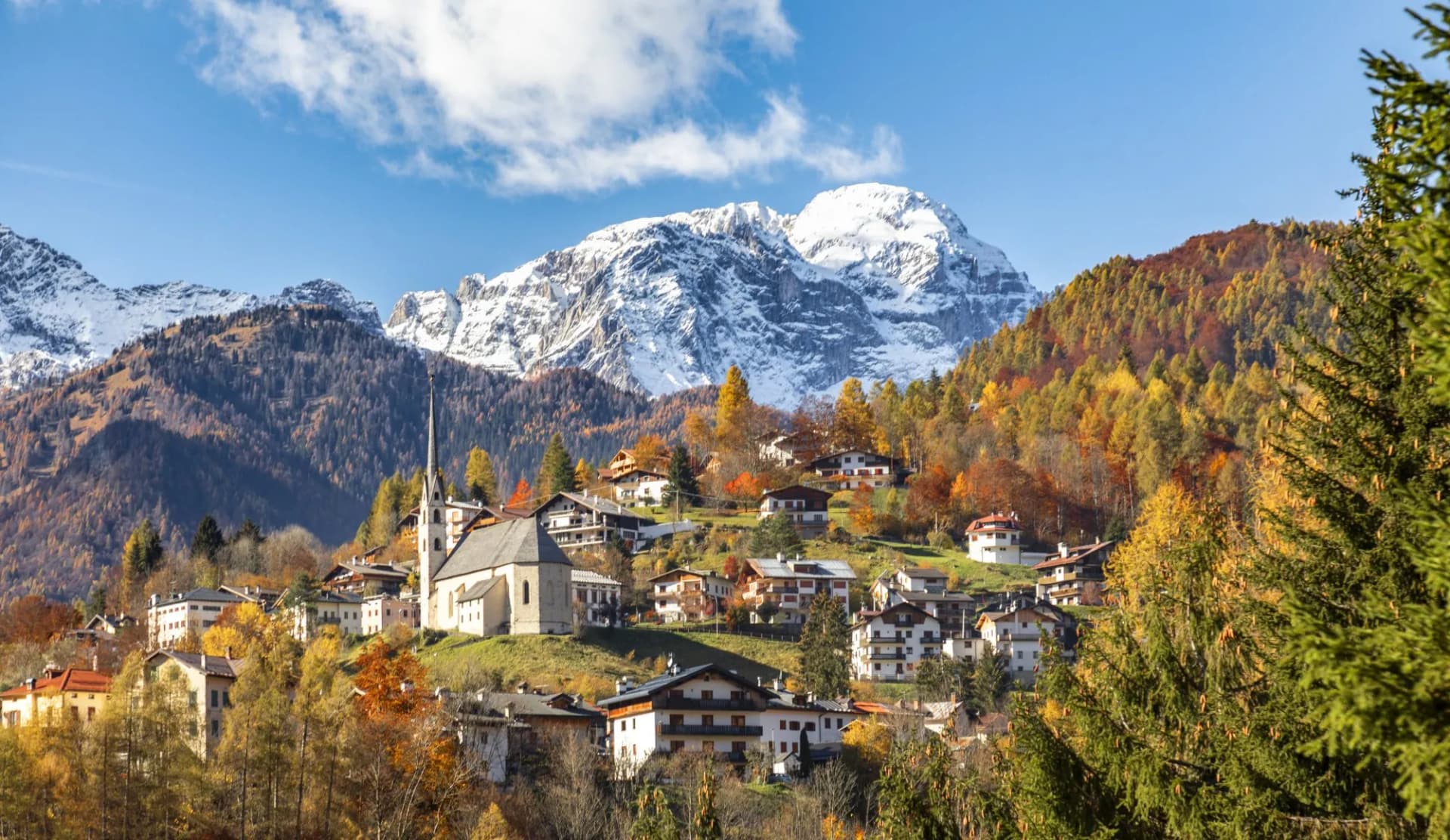 Alpine village of Val di Zoldo with colorful autumn trees and snow-capped mountains.