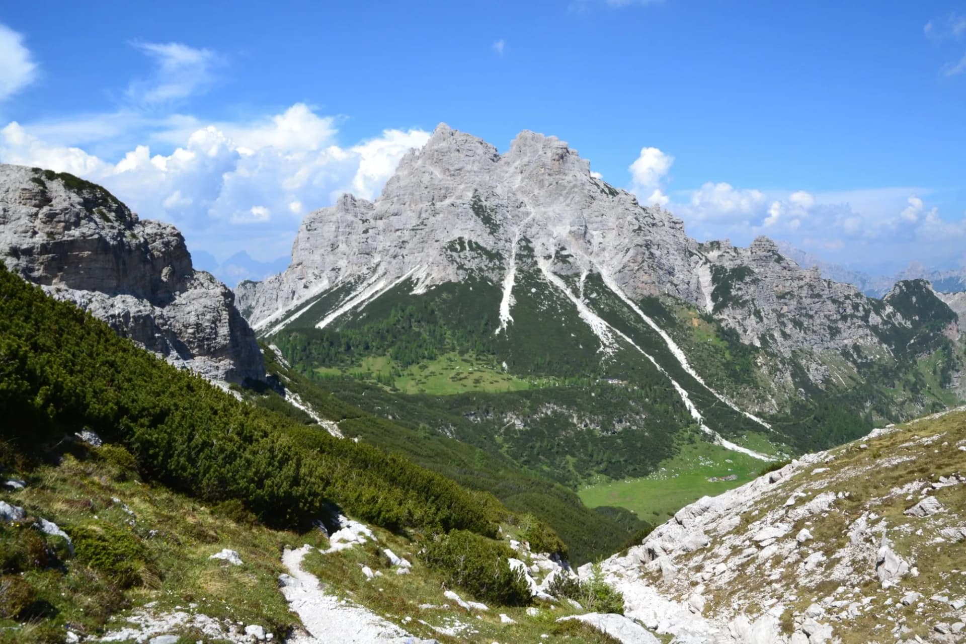 Rocky mountain peaks with green slopes under a bright blue sky with clouds, Cima Pramper.