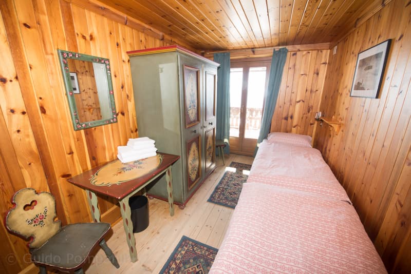 Single bedroom with wood paneling, painted furniture, and balcony door at Rifugio Lagazuoi.