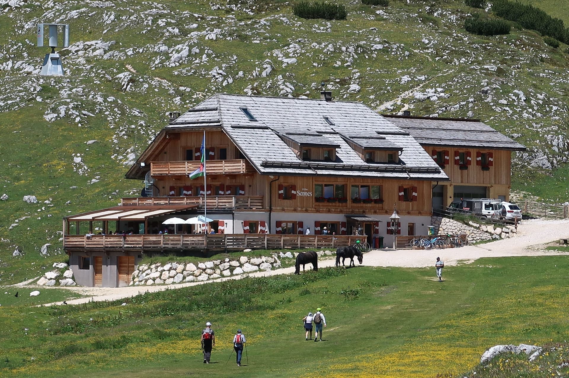 Rifugio Sennes wooden mountain hut with hikers and horses on grassy slope.