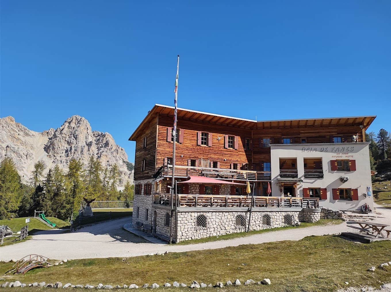 Rifugio Fanes mountain hut with wooden structure against rocky peaks and clear blue sky.