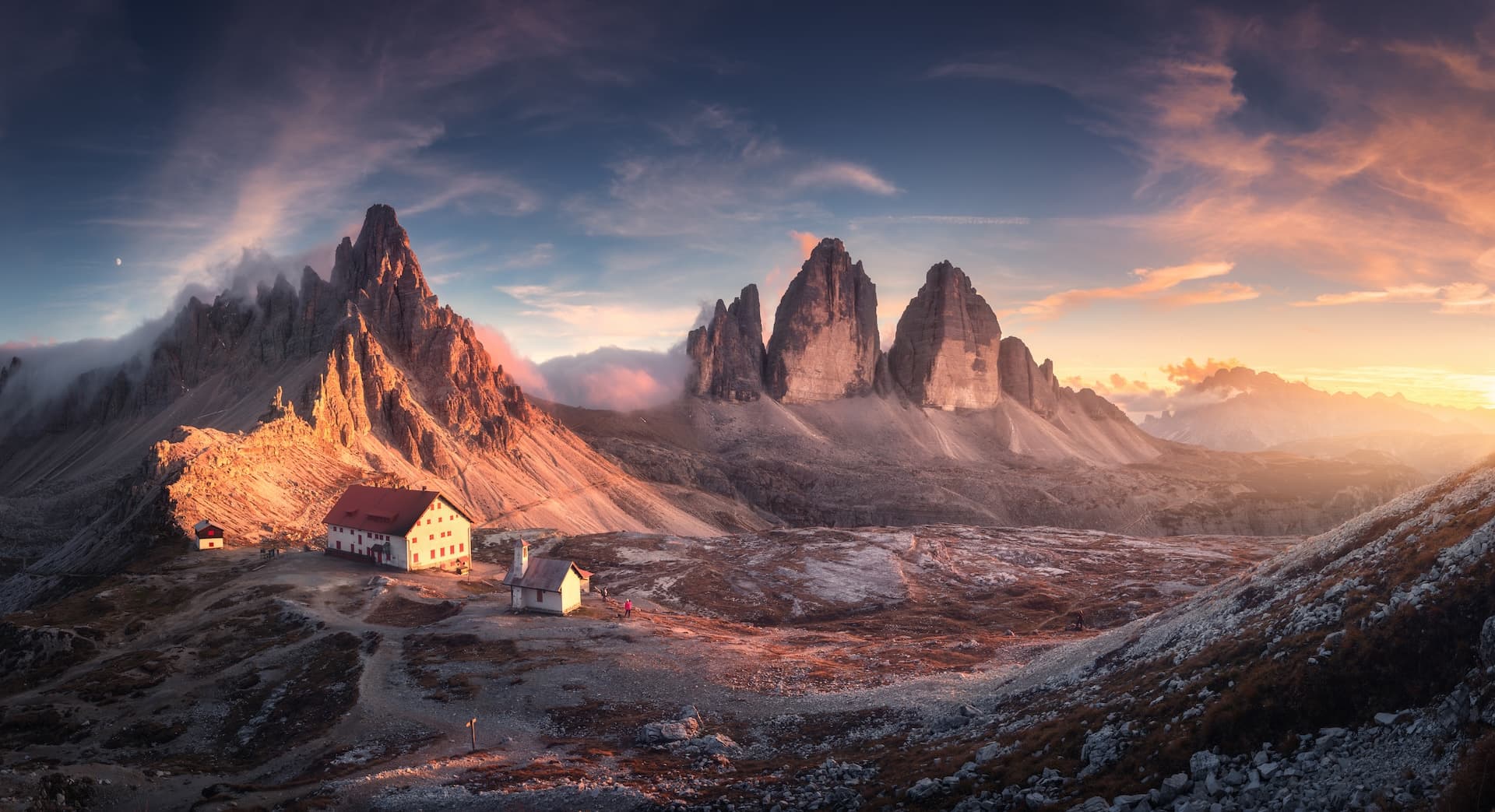 Mountains in Tre Cime park in Dolomites at sunrise with mountain huts below.