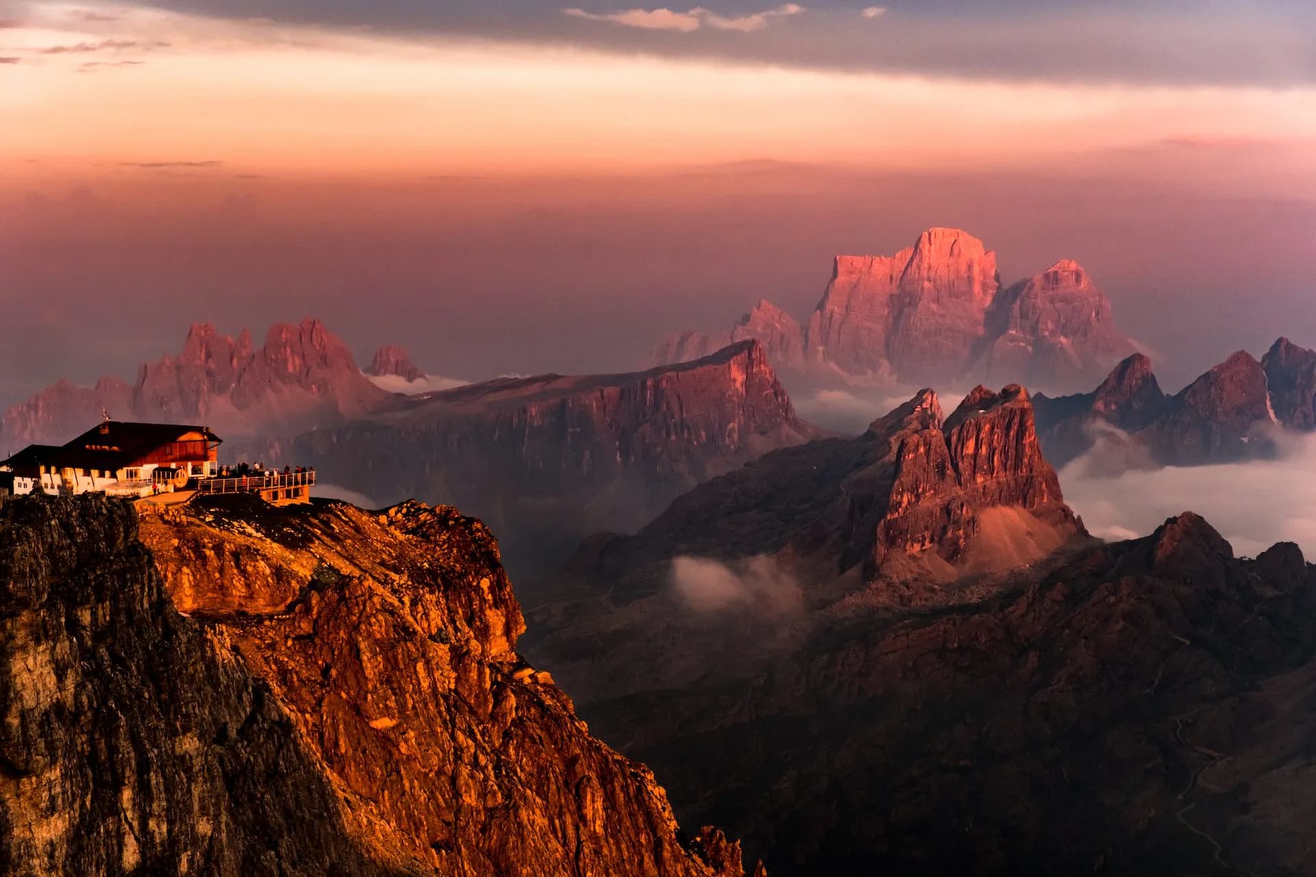 Rifugio Lagazuoi mountain hut perched on a cliff overlooking jagged peaks at sunset.