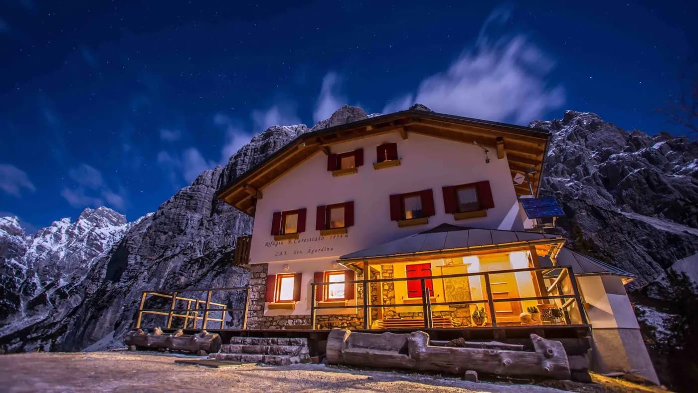 Rifugio Carestiato illuminated at night beneath snowy mountains and a starry sky