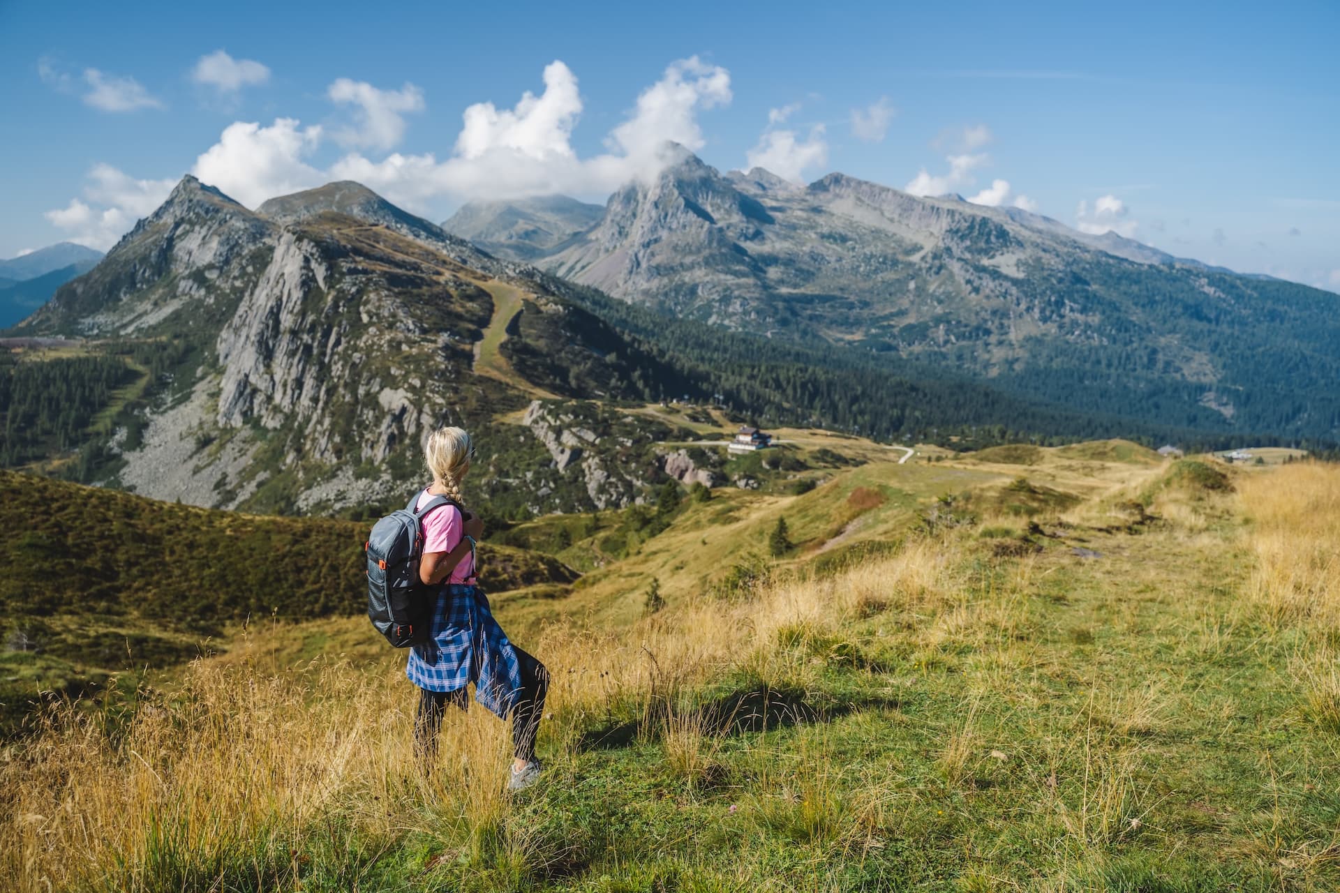 Hiker with backpack looking at rugged mountains near Passo Rolle in summer.
