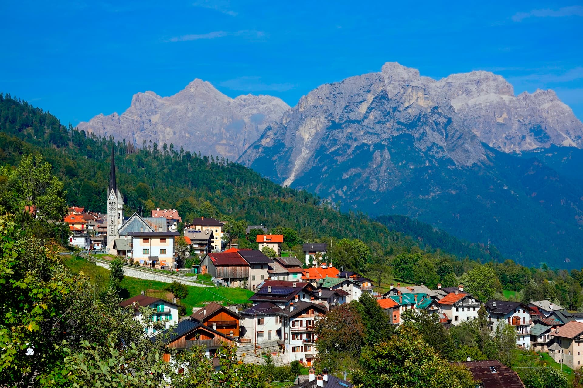 Alpine village of San Martino di Castrozza nestled on green hillside below rocky mountains.