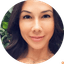 Close-up portrait of woman with dark hair and necklace against green foliage background.