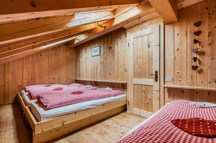 Attic bedroom in wooden hut with beds covered in red and white gingham duvets, Franz Kostner hut
