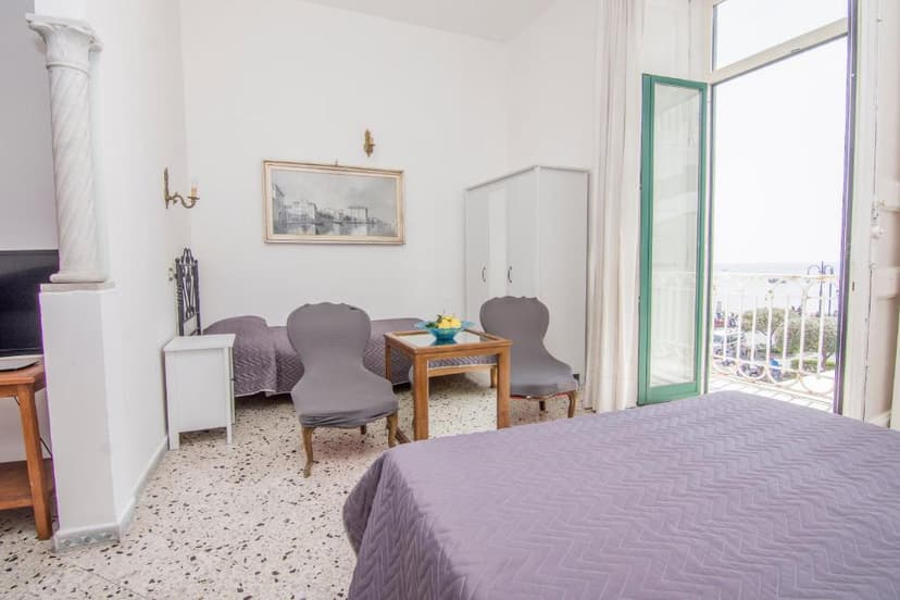 Hotel room with beds, chairs, and balcony view of the sea and coast.