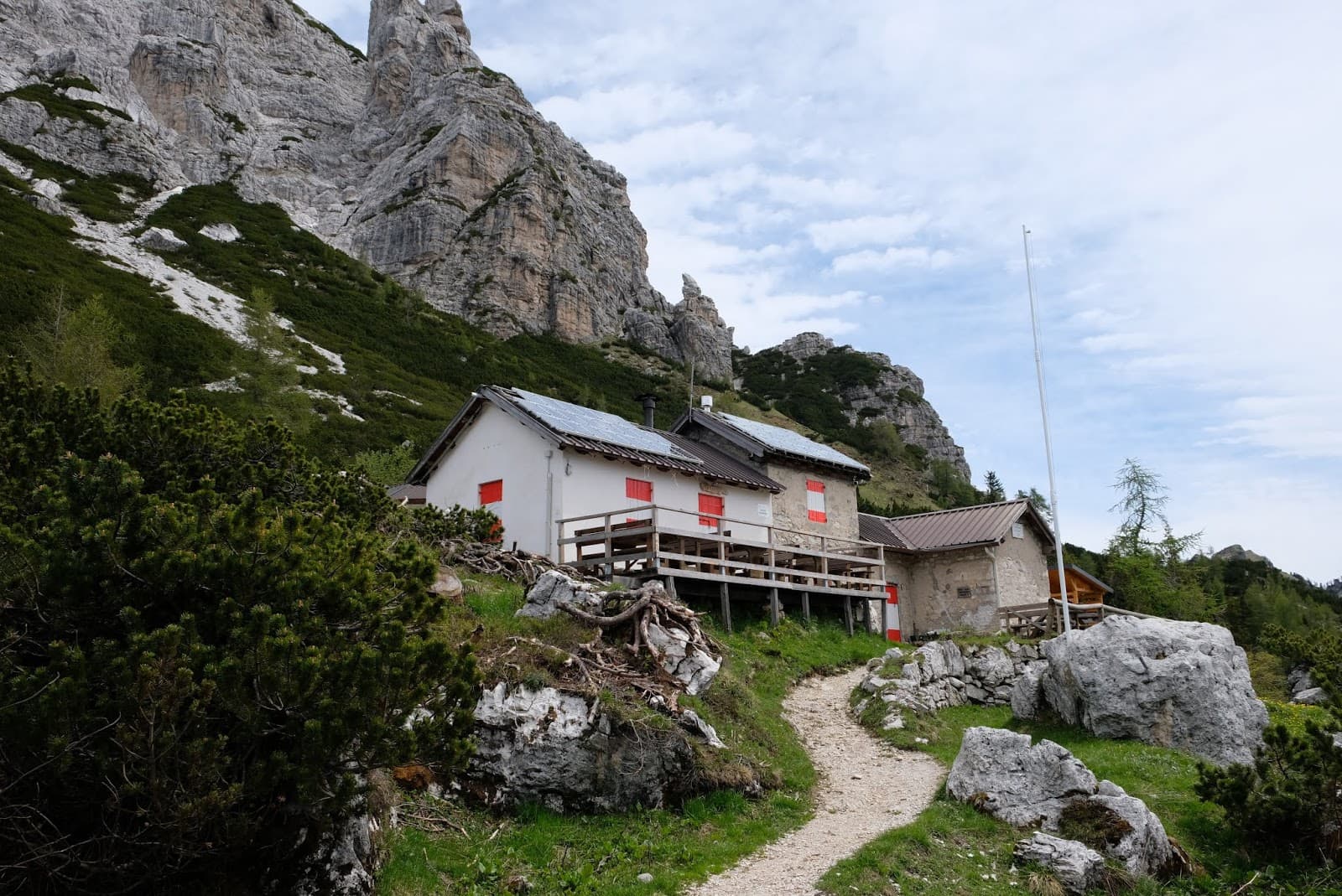 Rifugio Sommariva al Pramperet mountain hut below steep rocky cliffs with a hiking path.