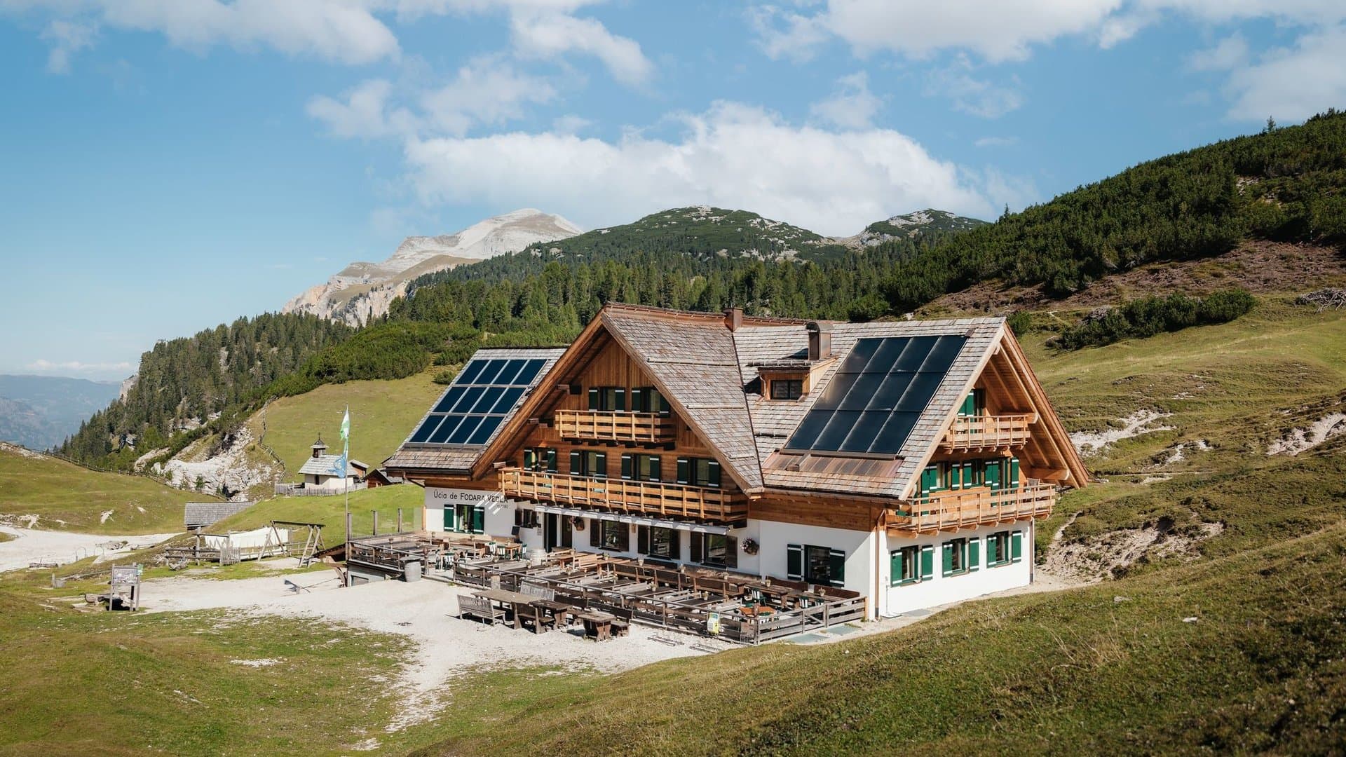 Rifugio Fodara Vedla mountain hut with solar panels in grassy alpine setting under blue sky.
