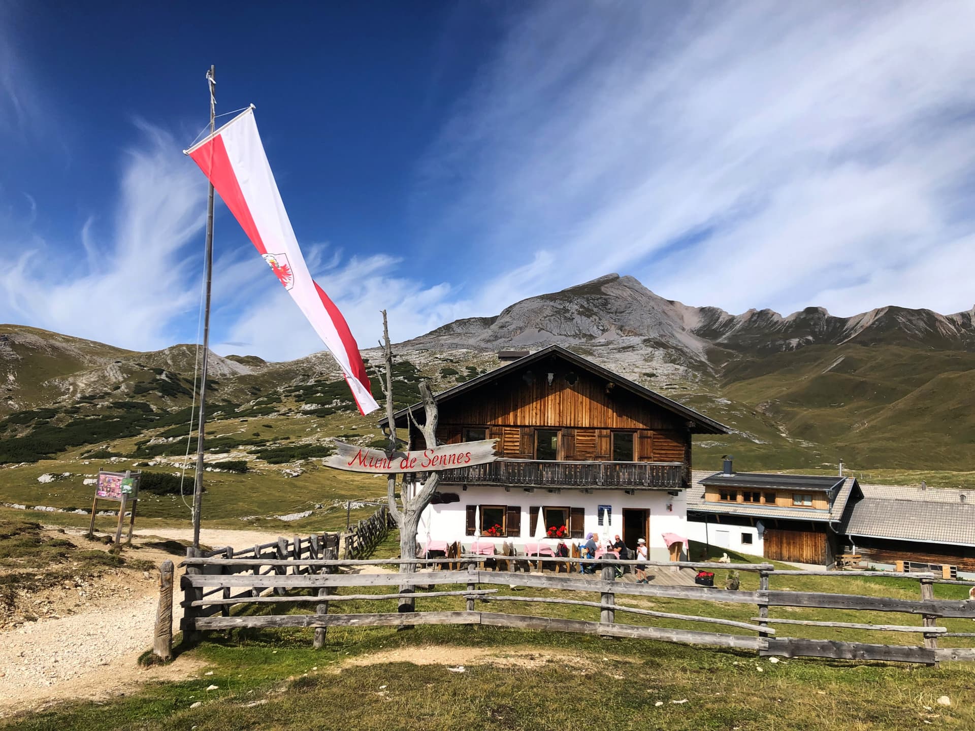 Rifugio Munt de Sennes mountain hut with Austrian flag flying under blue sky.