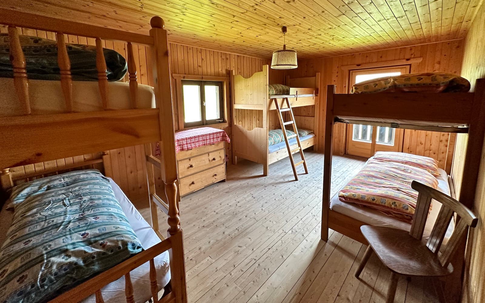 Bunk room interior with wooden walls, floors, and multiple wooden bunk beds at Rifugio Munt de Sennes.