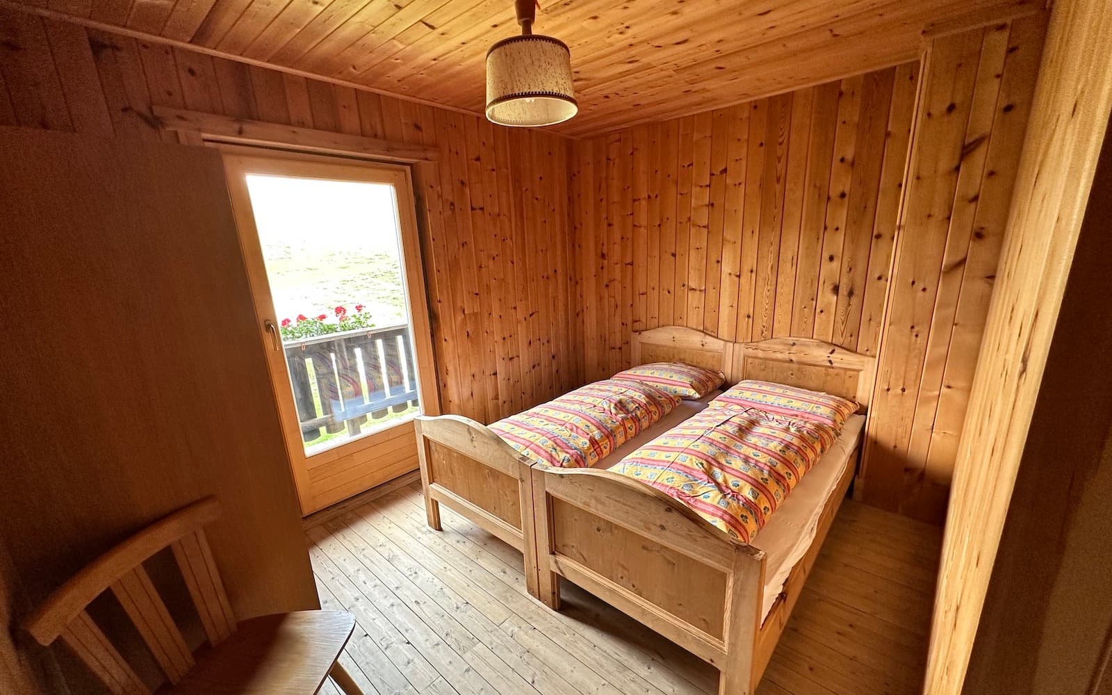 Twin beds in a wood-paneled room with a door leading to a balcony at Rifugio Munt de Sennes.