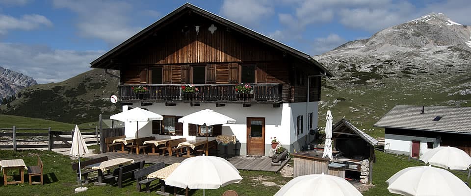 Rifugio Munt de Sennes mountain hut with outdoor seating and high alpine peaks.