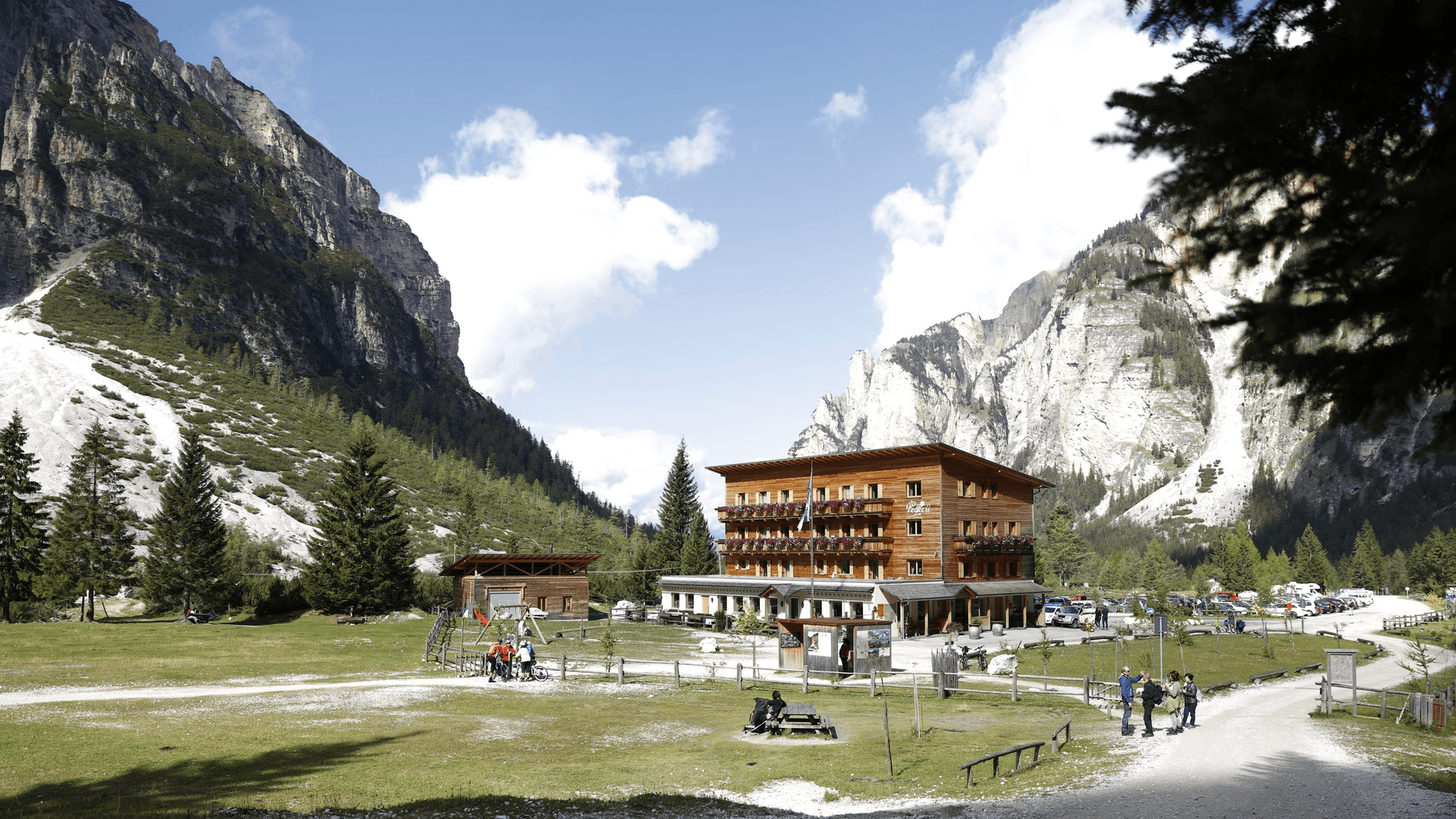 Berggasthaus Pederü hotel nestled between steep, rocky mountains with green slopes and pine trees.