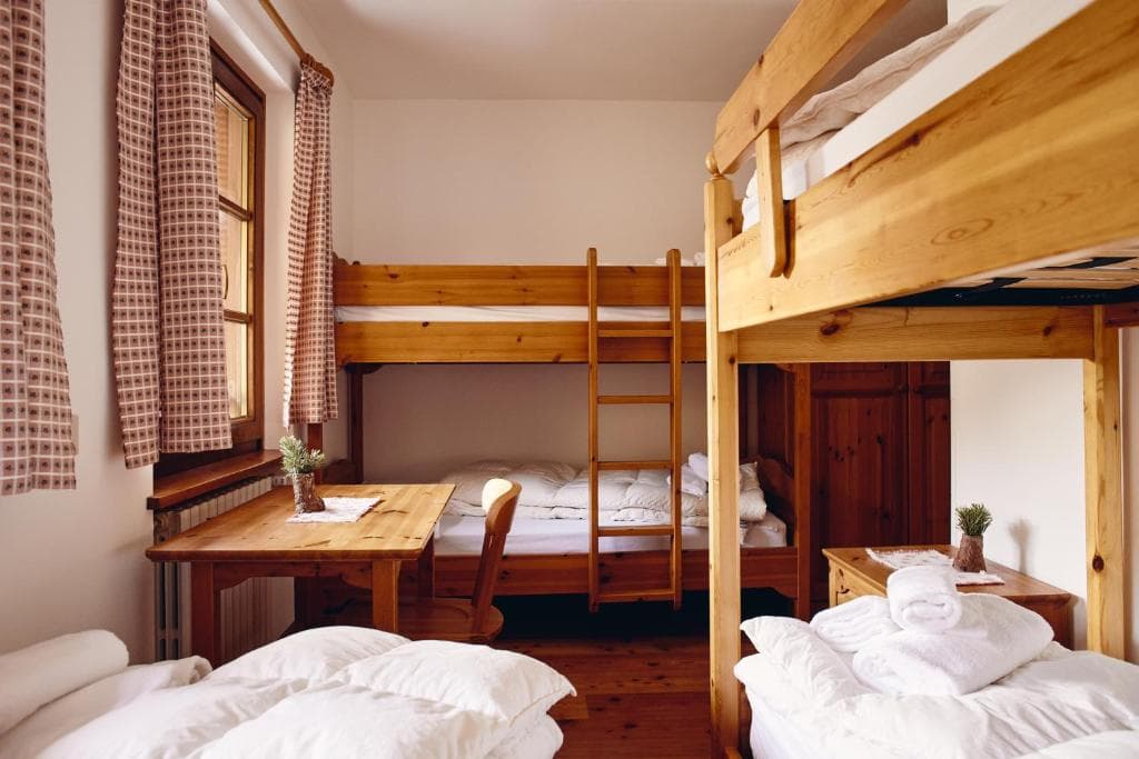 Bunk beds and wooden furniture in a simple Rifugio Malga Ra Stua dormitory room.