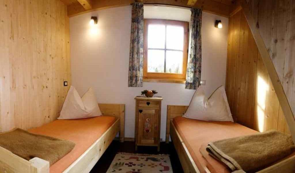 Twin bedroom with wood paneling, orange mattresses, and a window in an alpine setting.