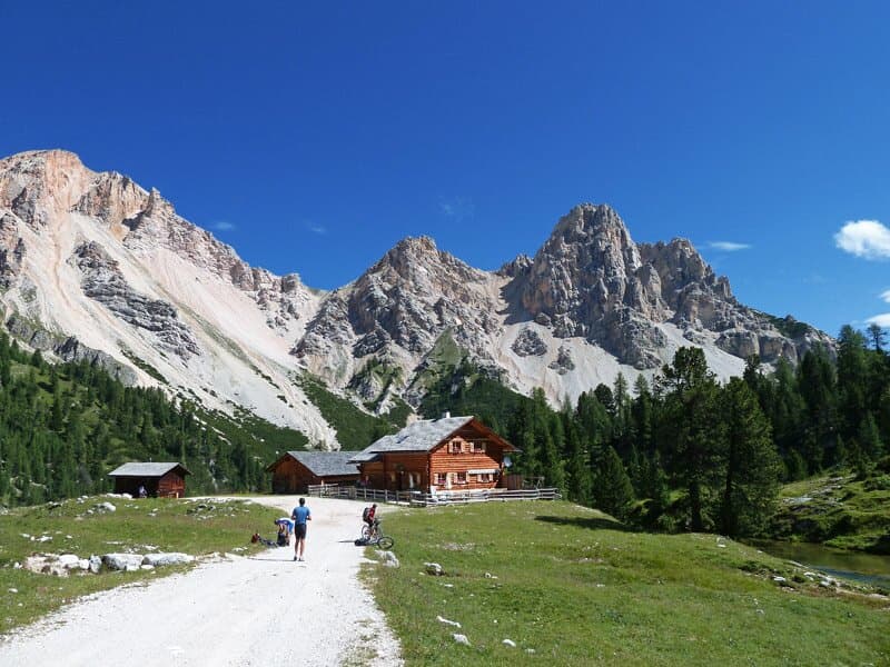 Hikers approaching wooden mountain huts below rugged peaks in the Fanes-Sennes-Braies Nature Park.
