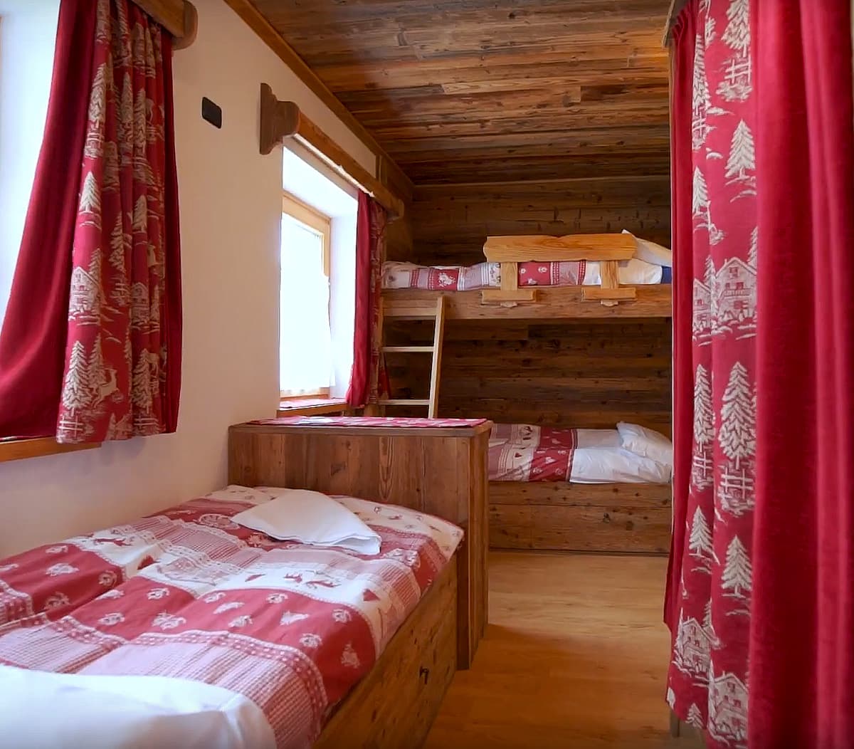 Rustic wooden mountain cabin bedroom with bunk beds and red patterned bedding at Rifugio Col Gallina.
