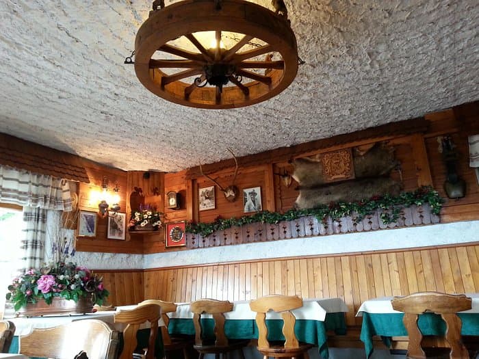Rustic restaurant interior with wood paneling, wagon wheel chandelier, and mounted animal hides near Rifugio Angelo Dibona.