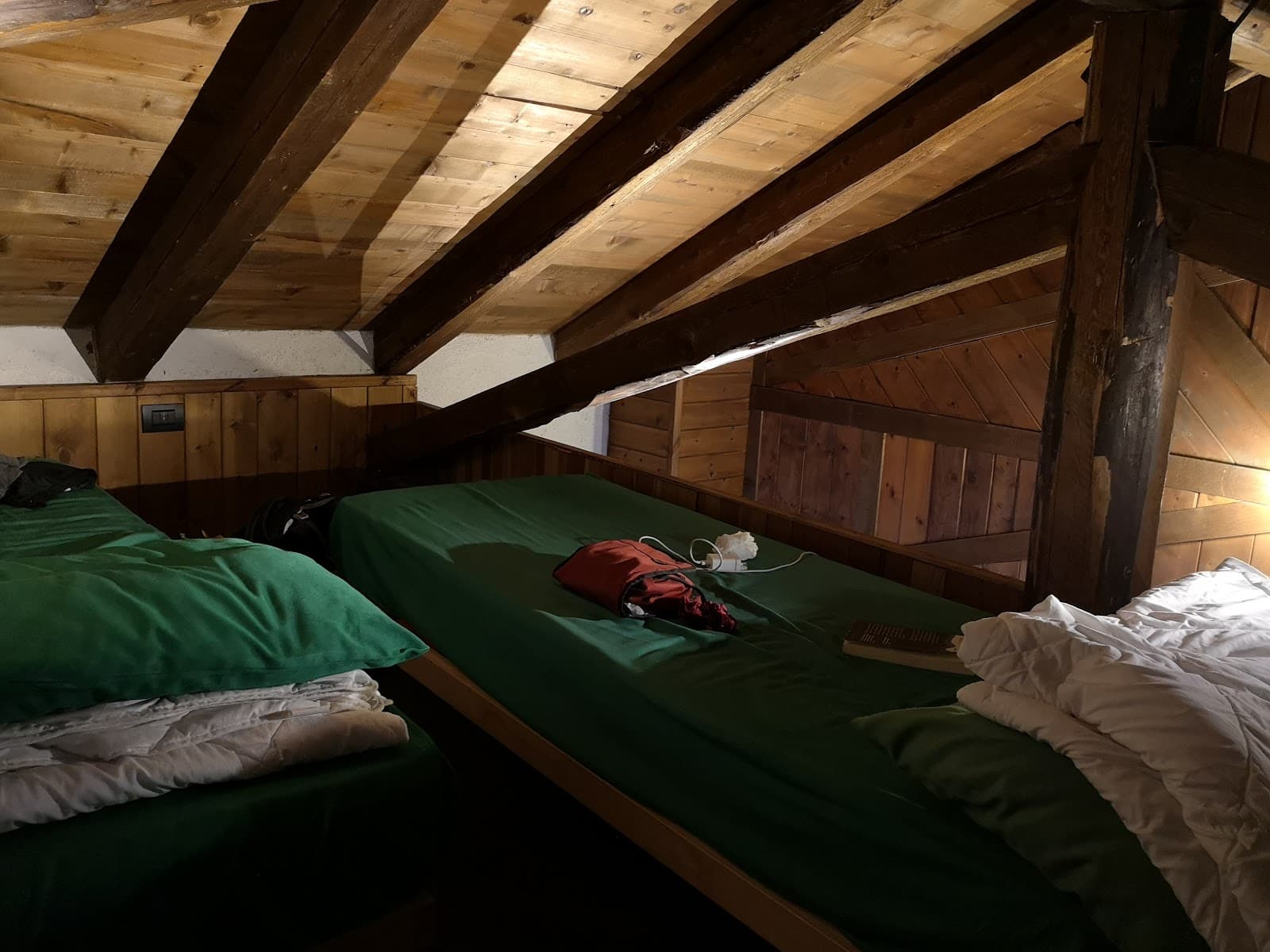 Bunk beds with green sheets in a rustic attic room with exposed wooden beams at Rifugio Angelo Dibona.