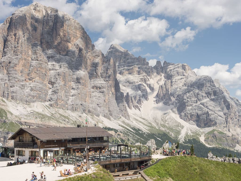 Rifugio Scoiattoli mountain hut with people relaxing below massive Dolomite peaks in summer.