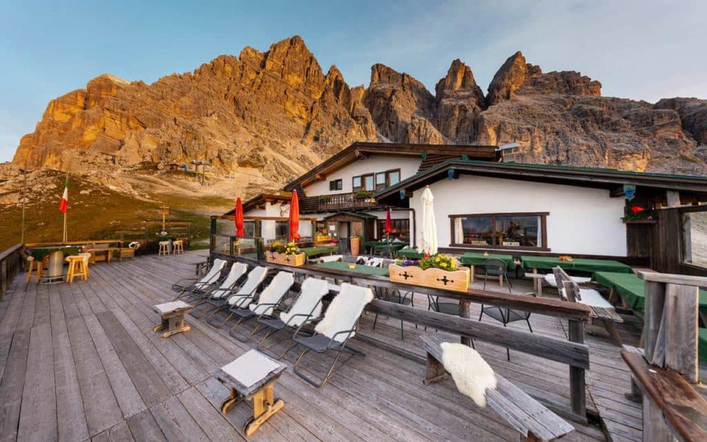 Rifugio Pomedes mountain hut terrace with sun loungers and jagged Dolomite peaks.