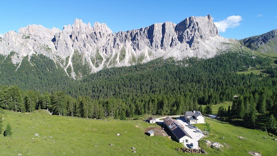 Malga Giau alpine hut nestled in green meadow below jagged Dolomite mountains.