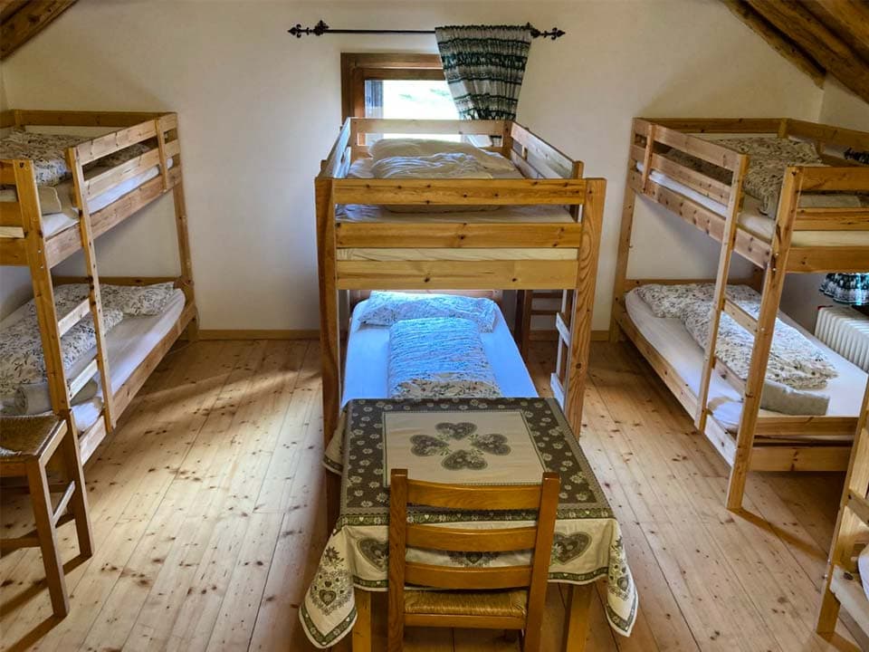 Bunk beds in a rustic room with wooden floors and a central table, Malga Giau.
