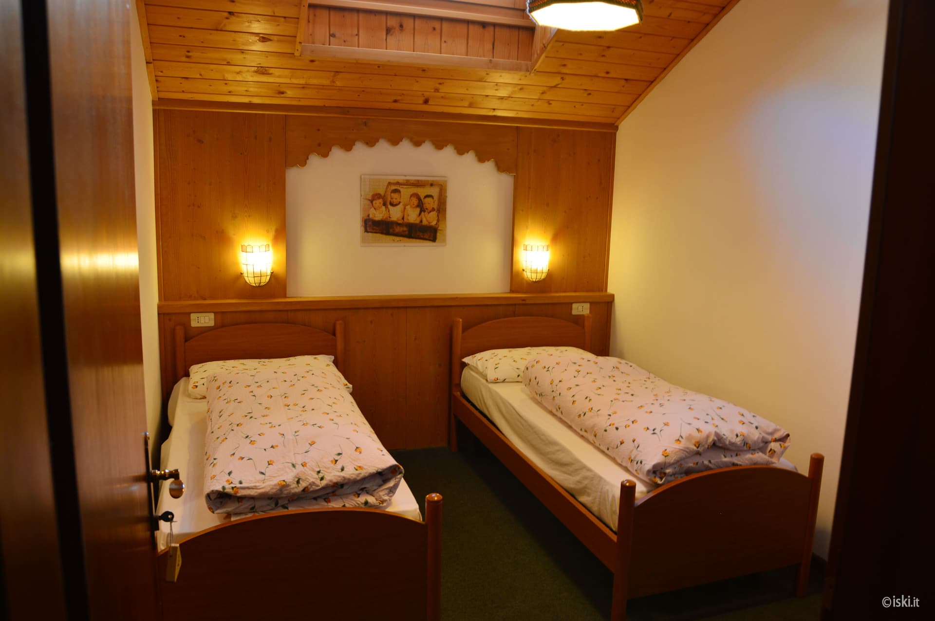 Twin bedroom with wooden paneling, two single beds, and warm wall sconces in Rifugio Fedare.