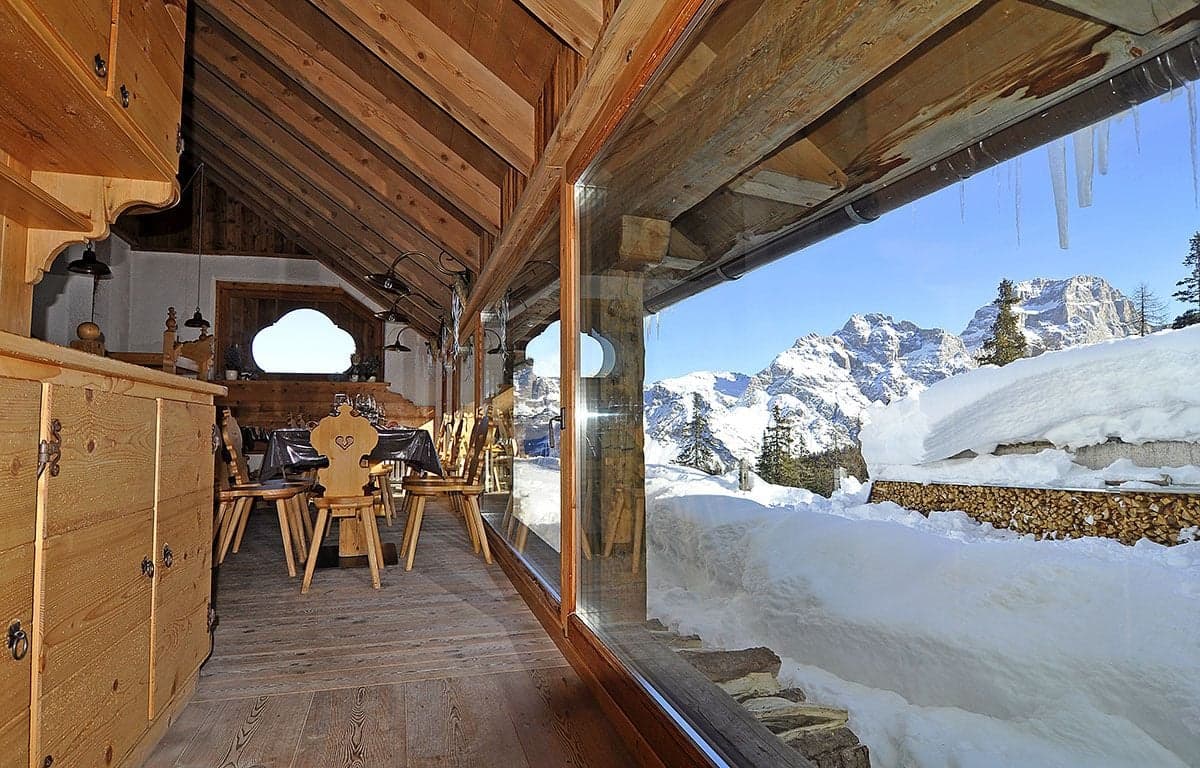 Rustic wooden interior with dining tables overlooking snow-covered mountains in winter.