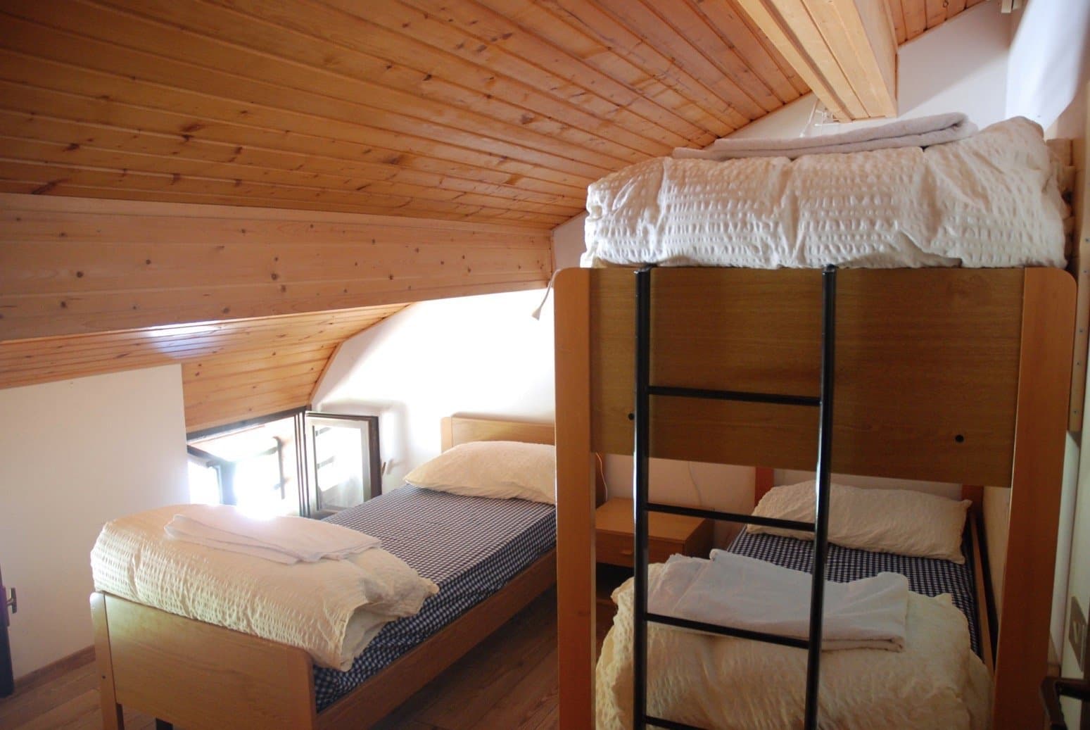 Bunk beds and single bed in attic room with wooden plank ceiling, Rifugio Aquilea.