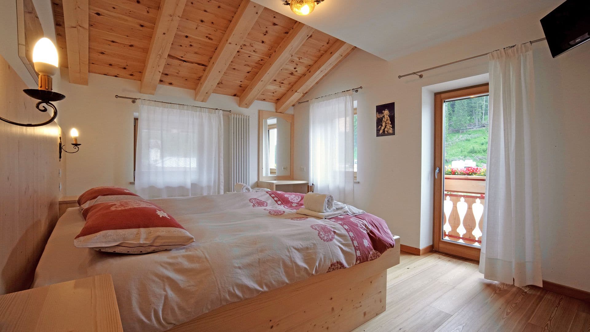 Bedroom with wood beam ceiling, light wood furniture, and balcony view of green hillside at Rifugio Palafavera.