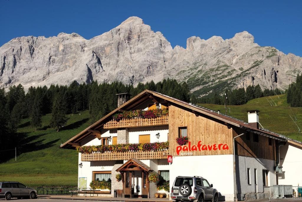 Rifugio Palafavera building with flower boxes against a backdrop of rugged gray mountains.