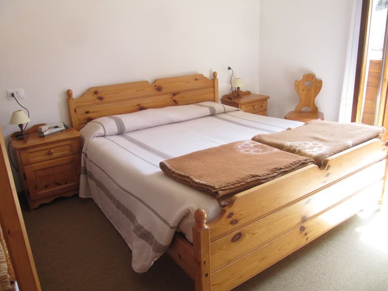 Wooden double bed with white and brown blankets in a bright room, Rifugio San Sebastian.