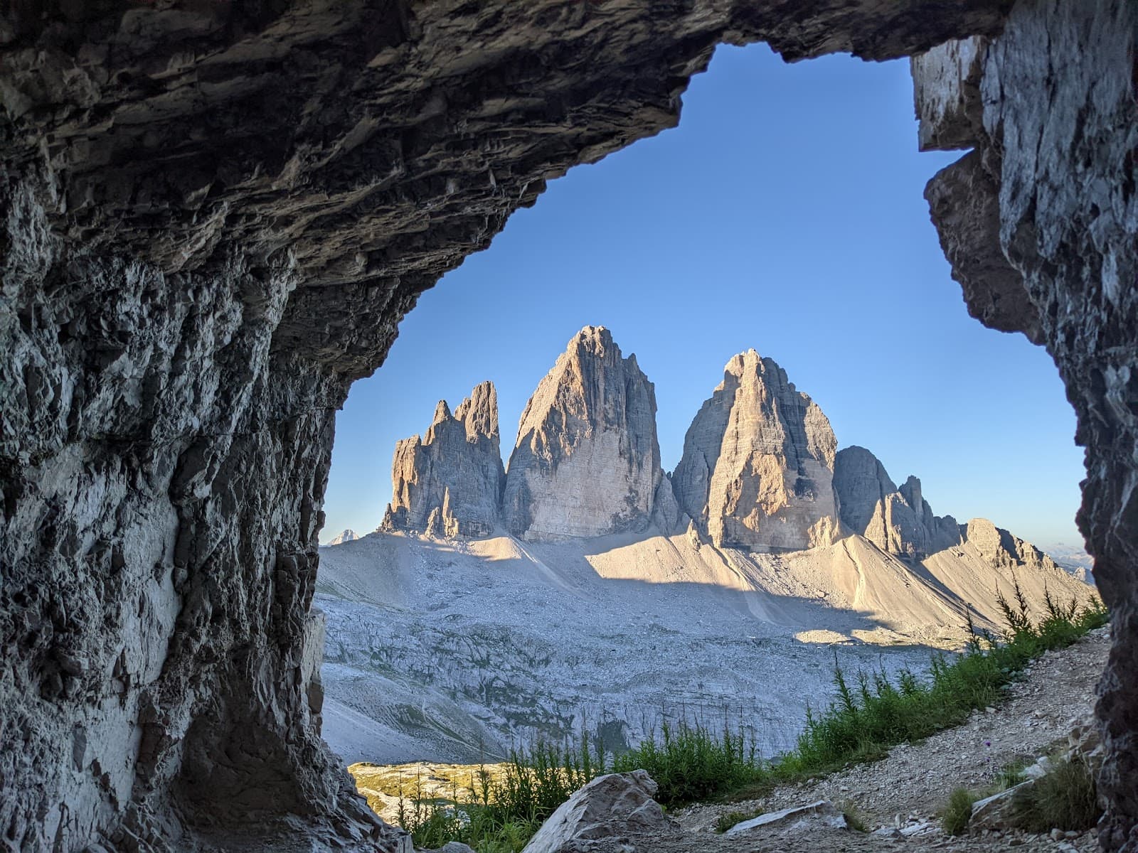 Tre Cime di Lavaredo mountains seen through a rocky cave opening under clear blue sky