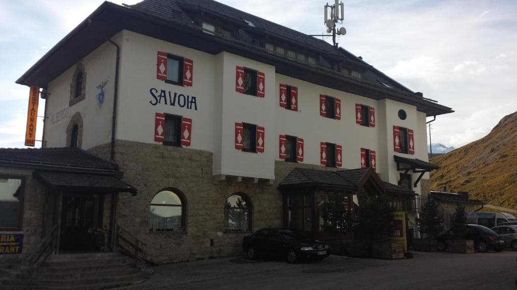Albergo Savoia hotel building with stone base and red shutters in a mountain landscape.
