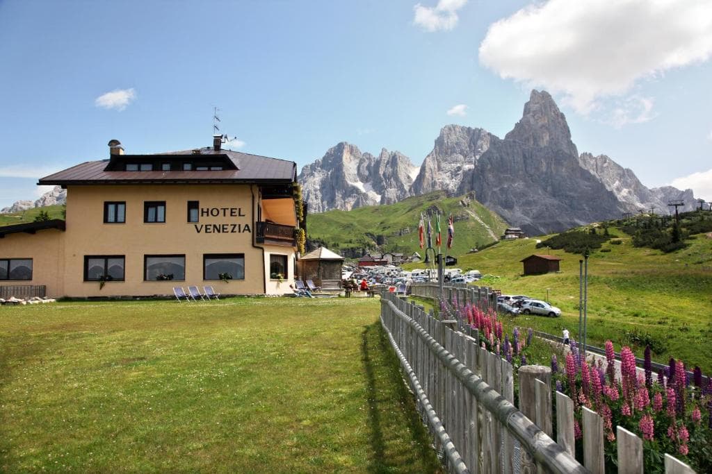 Hotel Venezia building in a mountain landscape with rocky peaks and green meadows.