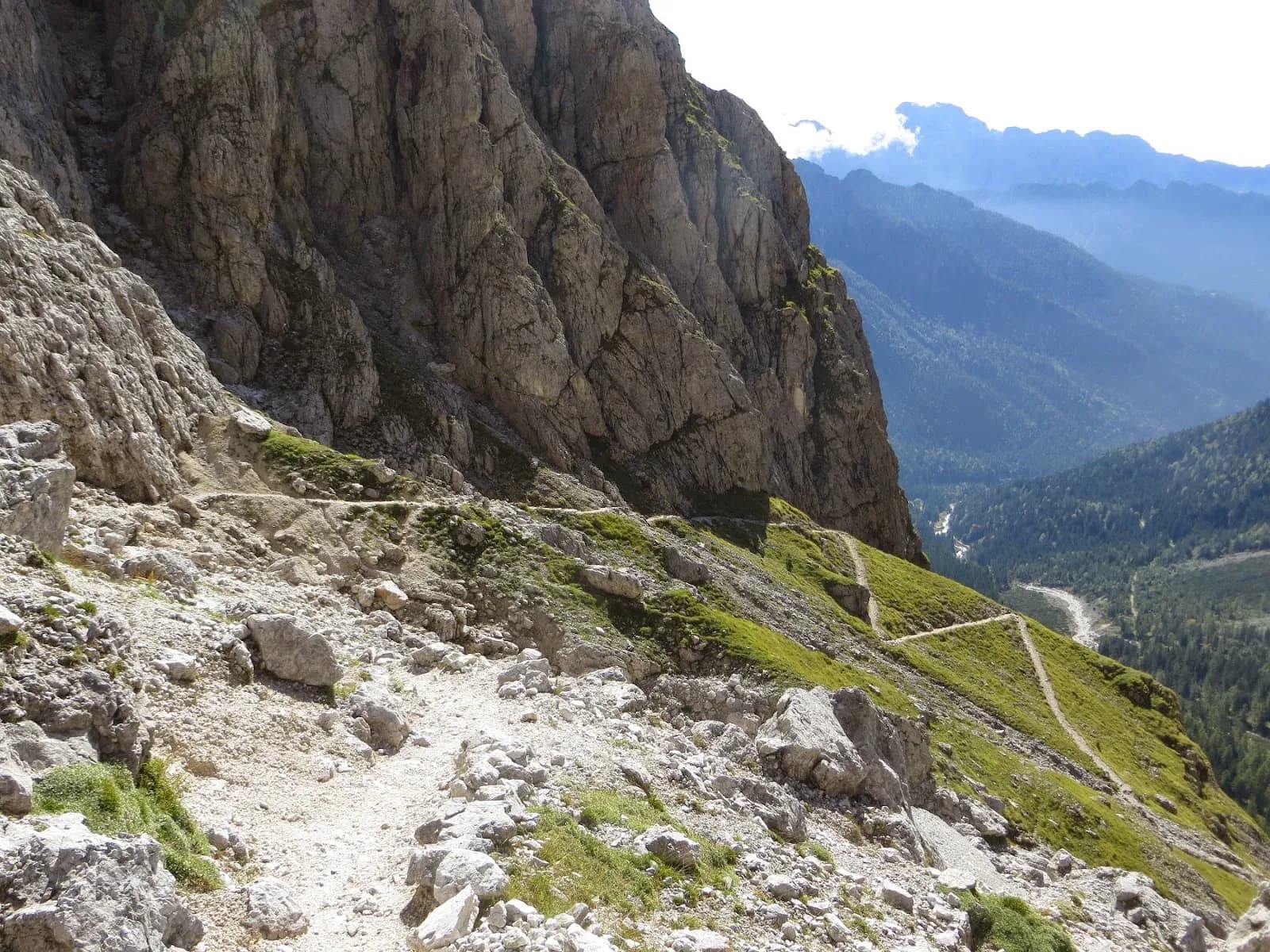 Hiking trail on a steep rocky slope in the Pale di San Martino mountains with a valley view below.