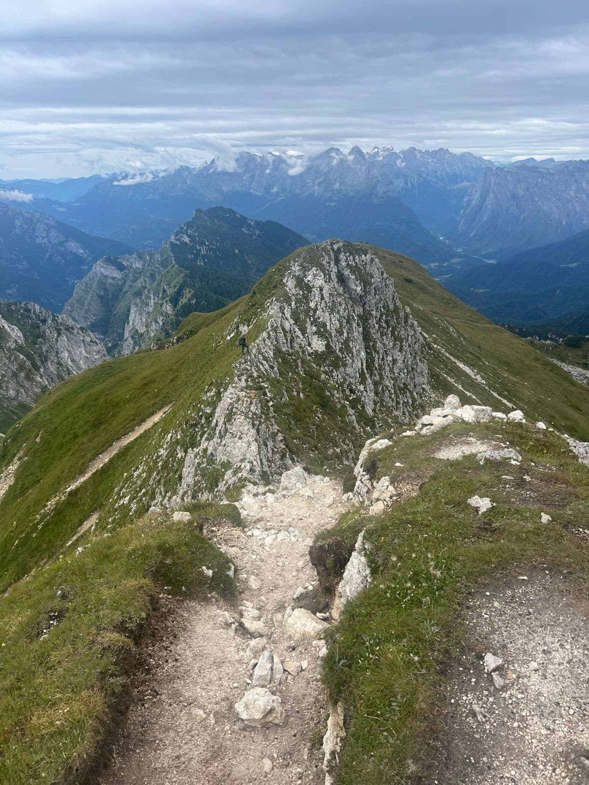 Hiker on a narrow rocky mountain ridge with panoramic alpine views.